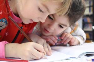 2 Kinder sitzen nebeneinander und schreiben.