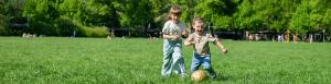 Zwei Kinder spielen Ball auf einer Wiese.
