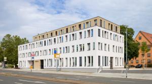 Haus mit weißer und hellbrauner Fassade vor leicht bewölktem Himmel und Bäumen