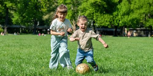Zwei Kinder spielen Ball auf einer Wiese.