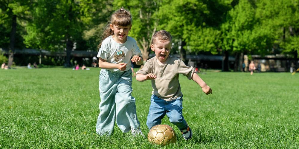 Zwei Kinder spielen Ball auf einer Wiese.
