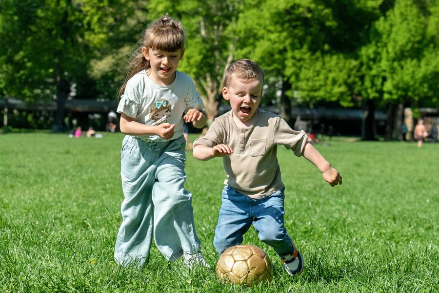 Zwei Kinder spielen Ball auf einer Wiese.