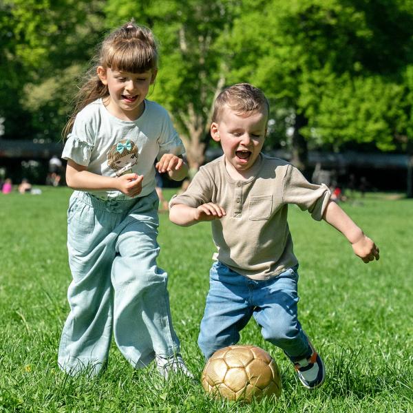 Zwei Kinder spielen Ball auf einer Wiese.
